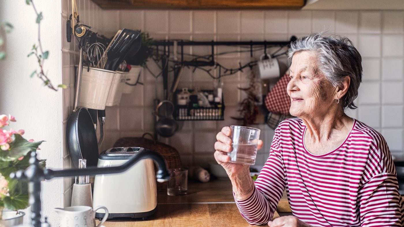 Ältere Dame mit einem Glas Wasser in der Küche